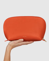 Hand holding a zippered pouch against a plain background.