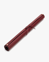 Rolled-up leather mat secured with straps against plain background