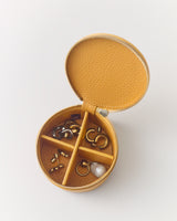 Round jewelry case with open lid showing compartments with earrings and rings inside.