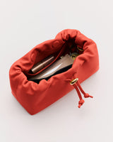 Open drawstring pouch with items inside including lipstick and compact.