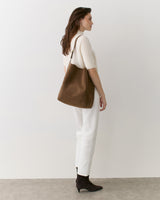 Person standing with a shoulder bag, wearing a short-sleeved top and pants, facing left.