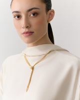 Person wearing a top with a gold necklace and earrings.