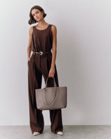 Person standing with large handbag wearing sleeveless top and trousers.