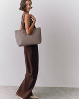 Person in a long dress holding a tote bag stands against a plain background.