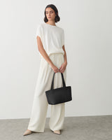 Person in loose outfit holding tote bag standing on gray floor.