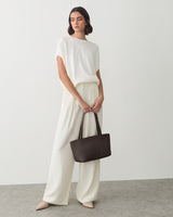 Person stands holding a handbag, wearing a short-sleeve top and wide-leg pants.