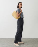 Person holding bag on shoulder stands in relaxed pose wearing casual clothes.