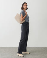 Person in casual outfit holding a handbag over shoulder, standing against plain background.