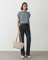 Person wearing a t-shirt and jeans holding a bag, standing indoors.