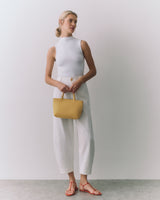 Person standing holding a small handbag, wearing a sleeveless top and pants.