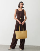 Woman in sleeveless top and pants holding a large handbag.