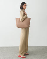Person standing with a large tote bag on their shoulder, facing sideways in a minimal setting.