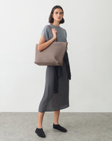 Woman in a dress holding a large shoulder bag, with a jacket tied around her waist.