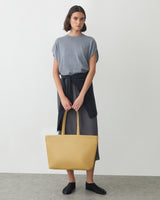 Person standing, holding a large tote bag, with a shirt tied around the waist.