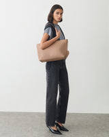 Person holding a large bag, wearing a t-shirt, pants, and heels.