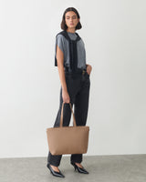 Person wearing casual clothes holding a tote bag in one hand.