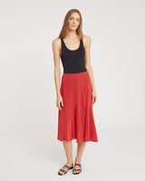 Person wearing a sleeveless top and long skirt, standing in a plain setting.