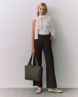 Person in sleeveless top and pants, holding a large handbag with a scarf over shoulders.