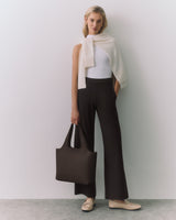 Woman standing with arms relaxed, wearing a top, pants, and holding a tote bag.