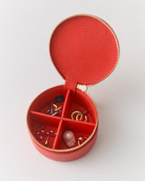 Round jewelry case with open zipper, divided into sections with various jewelry inside.