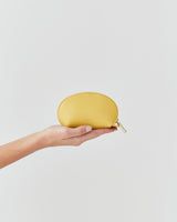Hand holds a small half-moon pouch against a plain background.