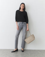 Person standing with a handbag, wearing a sweater, jeans, and shoes.