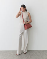 Person standing, wearing sleeveless top and trousers, holding shoulder bag.