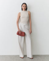 Person in a sleeveless top and wide-leg pants holds a clutch.