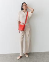 Person standing with a red crossbody bag, wearing a collared shirt and pants.