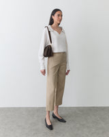 Person in long sleeve shirt, pants, and flats with shoulder bag in simple setting.