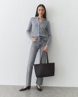 Person in casual outfit with tote bag stands against plain background.