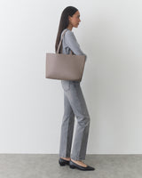 Person standing with large tote bag wearing jeans and shoes.