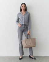 Person stands with neutral expression, wearing cardigan and jeans, holding a tote bag.