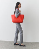 Person in profile view holding large tote bag, wearing long-sleeve shirt and jeans.
