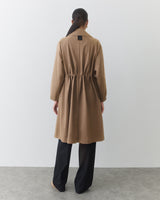 Person wearing a long coat and wide-leg pants, standing facing away.