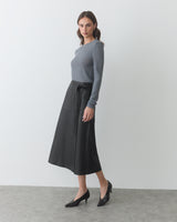 Person in long-sleeve top, midi skirt, and heels standing indoors.
