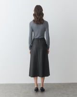 Person facing wall wearing long-sleeve shirt and long skirt.