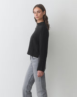 Person wearing a long-sleeve top and jeans, standing sideways.