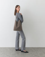 Person carrying shoulder bag, wearing long-sleeve shirt and pants, standing sideways.