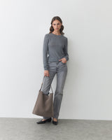 Person standing with a large bag wearing a long-sleeve shirt and jeans.