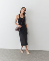 Person in sleeveless top and skirt with a crossbody bag, standing against a plain backdrop.