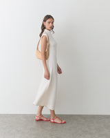 Person in long dress carrying a shoulder bag and wearing sandals.