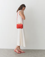 Person in sleeveless dress with shoulder bag and sandals stands on concrete floor.