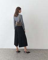 Person standing sideways, wearing long-sleeve top, culottes, heels, and shoulder bag.