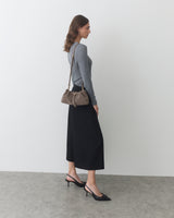 Woman standing sideways with shoulder bag and wearing a long skirt and heels.
