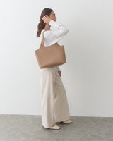 Person carrying a large shoulder bag, wearing a long-sleeve top and wide-leg pants.