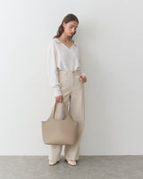 Person holding a large handbag, wearing a long-sleeve top and wide-leg pants.