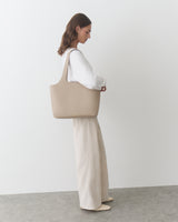 Person in a long-sleeve top and wide-leg pants holding a large shoulder bag.