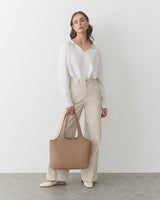 Person in a sweater and pants holding a handbag.