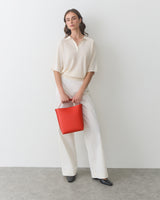 Person in relaxed outfit holding a handbag, standing against a plain background.
